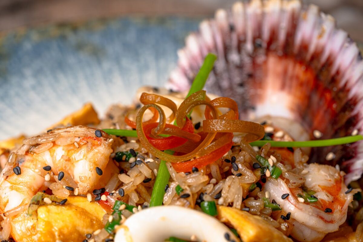 Close-up of shrimp fried rice garnished with vegetables and served with a decorative seashell.